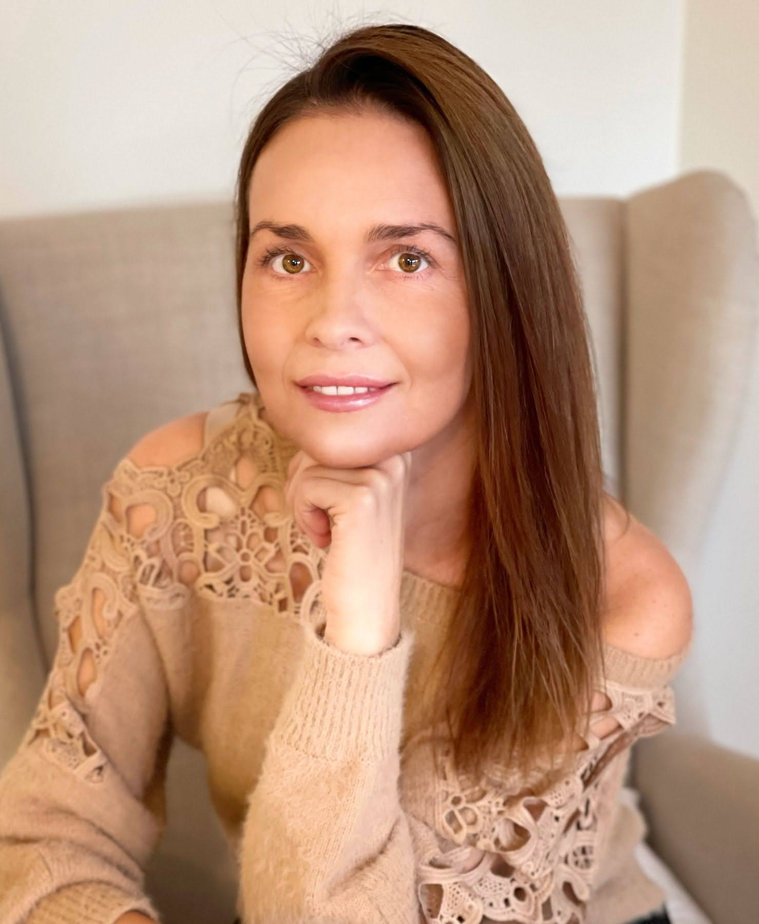 Woman wearing a beige sweater sitting on a couch.