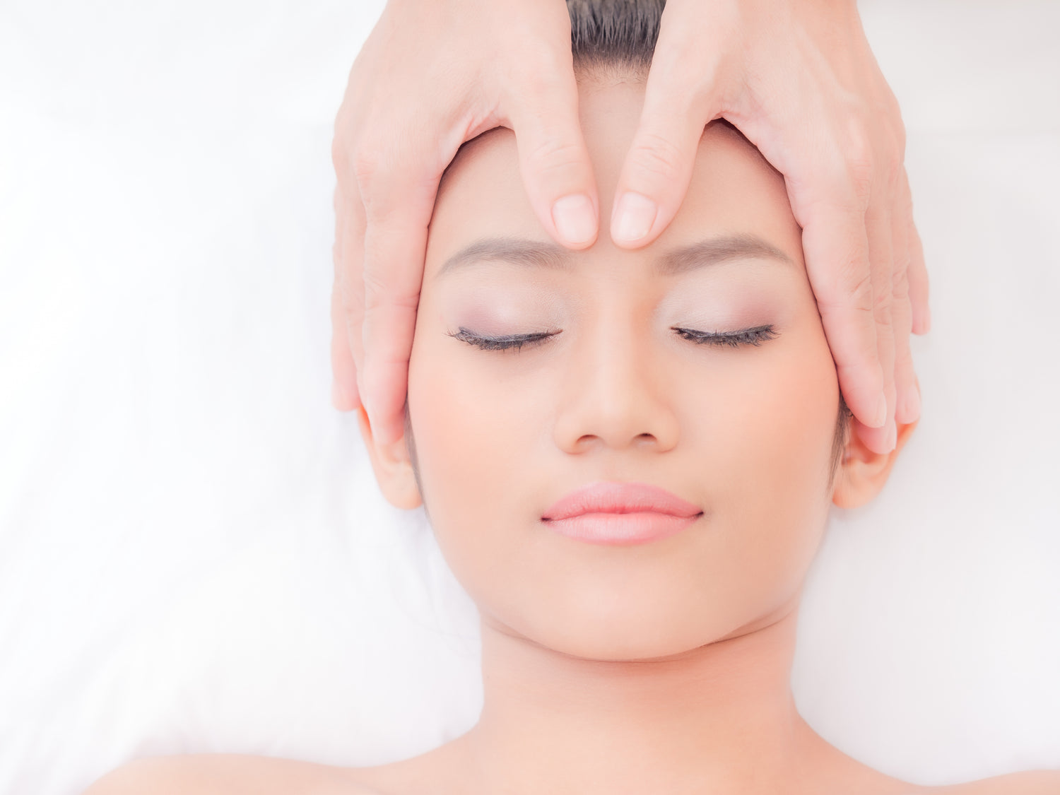 A relaxed woman lying in a serene setting while receiving a gentle face massage at Face by Greethel, enjoying the rejuvenating, anti-aging effects.