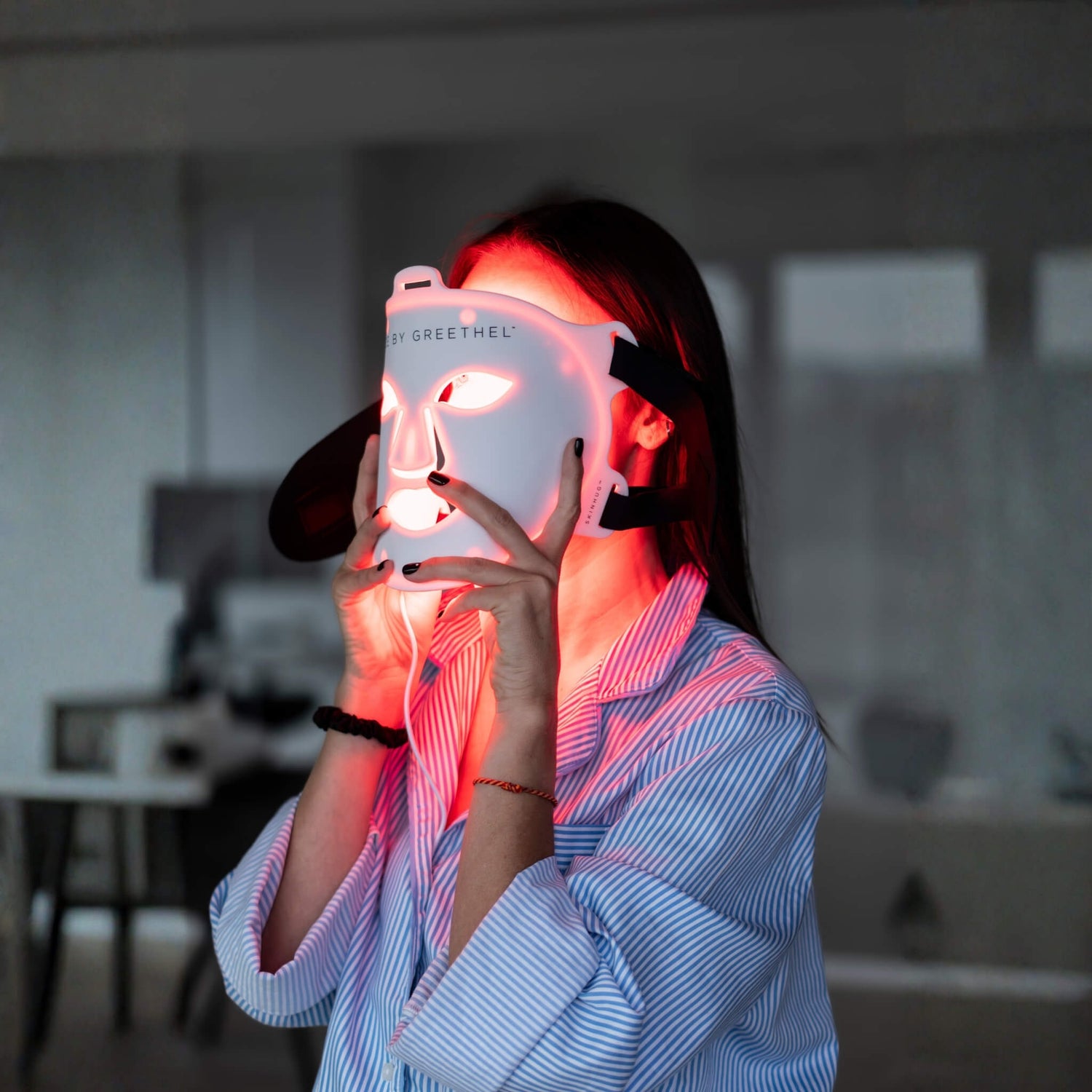 Person holding a light therapy mask with a blurred indoor background