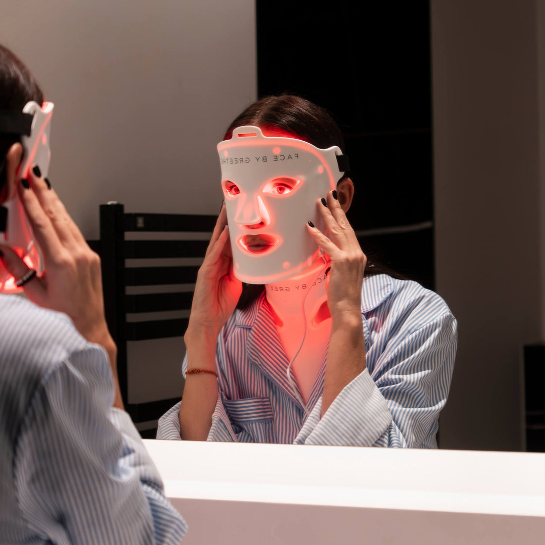 Person using a red light therapy mask in front of a mirror