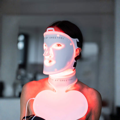 Person wearing a LED face and neck mask with visible branding indoors.