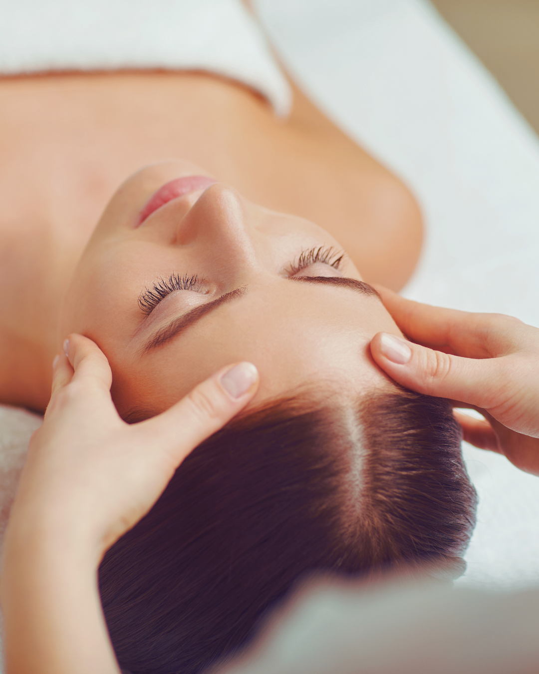 A woman receiving a face-lifting massage in a serene spa setting. A therapist’s hands gently lift and massage her skin using strokes, promoting relaxation and rejuvenation. 